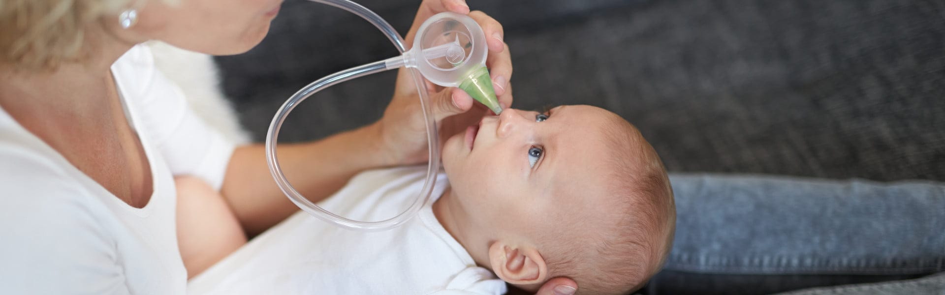 Kobieta oczyszcza nosek niemowlęcia za pomocą ustnego aspiratora do nosa Nosiboo Eco