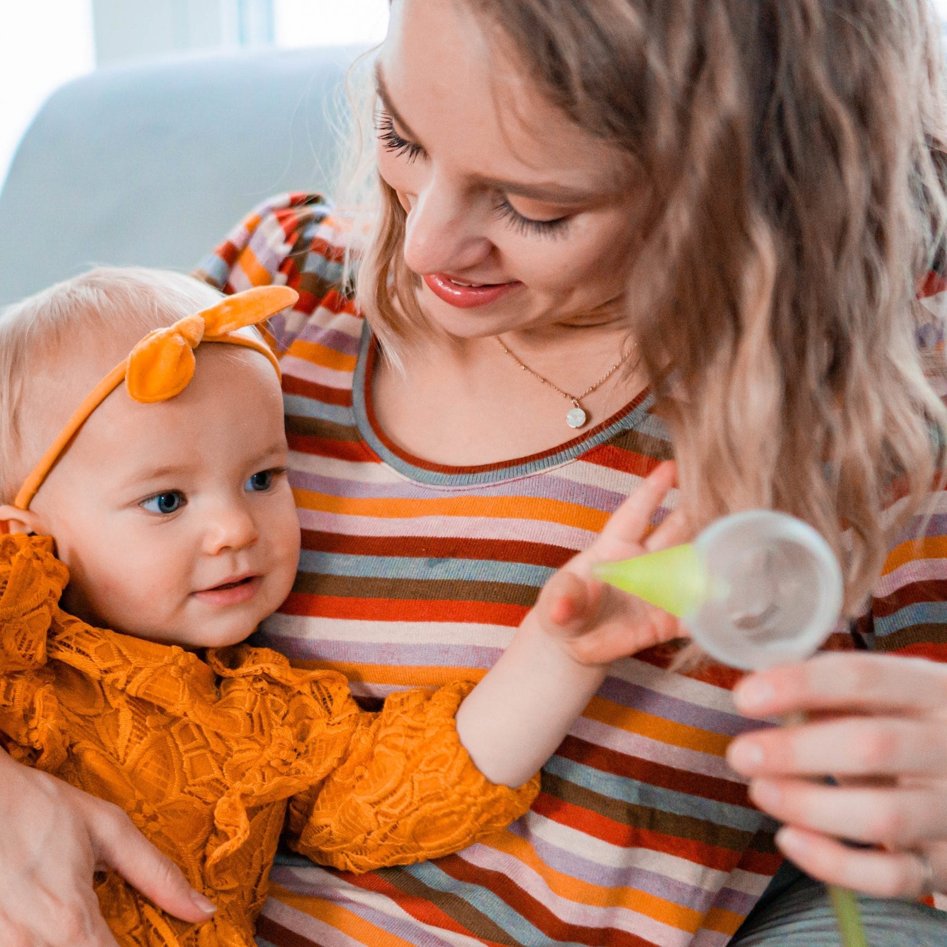 Mama z córką siedzi w fotelu, w ręce trzyma elektryczny aspirator do nosa Nosiboo Pro