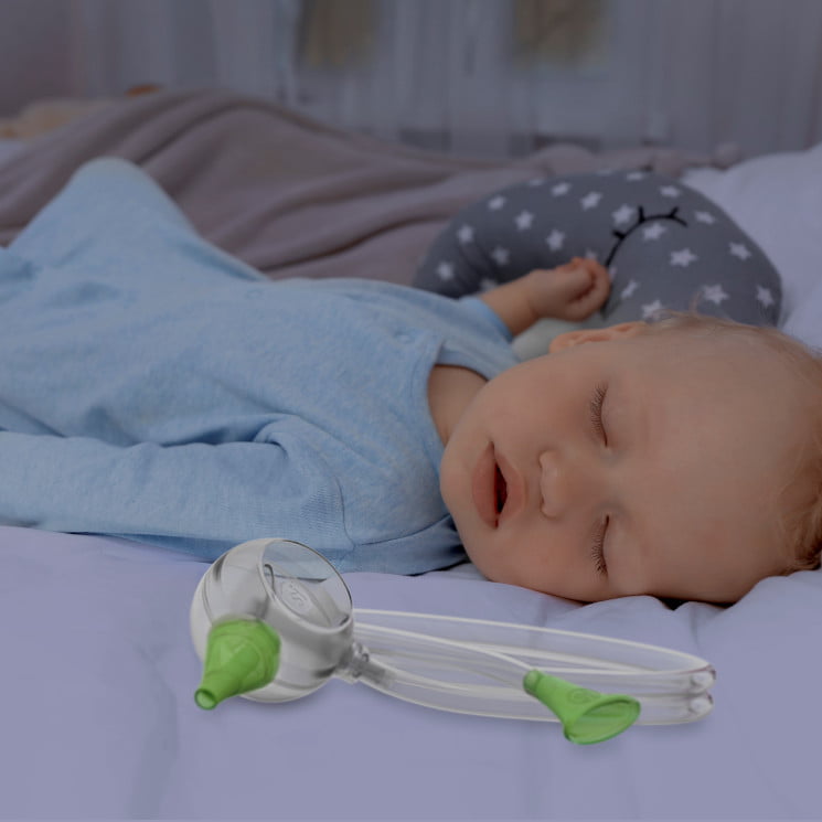 A baby boy sleeping peacefully in his bed next to the Nosiboo Eco Manual Nasal Aspirator