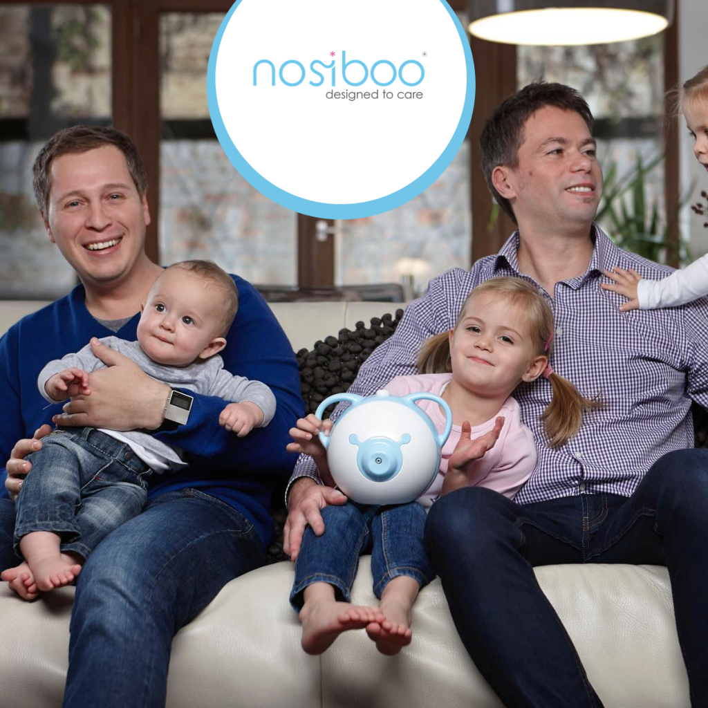 Two fathers, inventors of the Nosiboo products, sitting on a couch with their children and smiling
