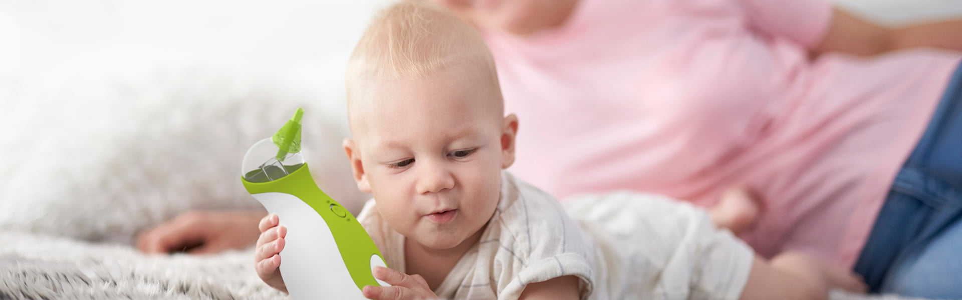 A woman and a baby boy lying on a carpet while holding the Nosiboo Go Portable Nasal Aspirator