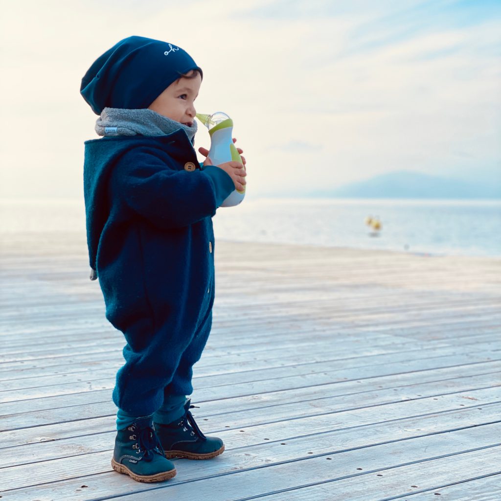Chłopiec nad brzegiem morza zimą, w ręce trzyma przenośny elektryczny aspirator do nosa Nosiboo Go