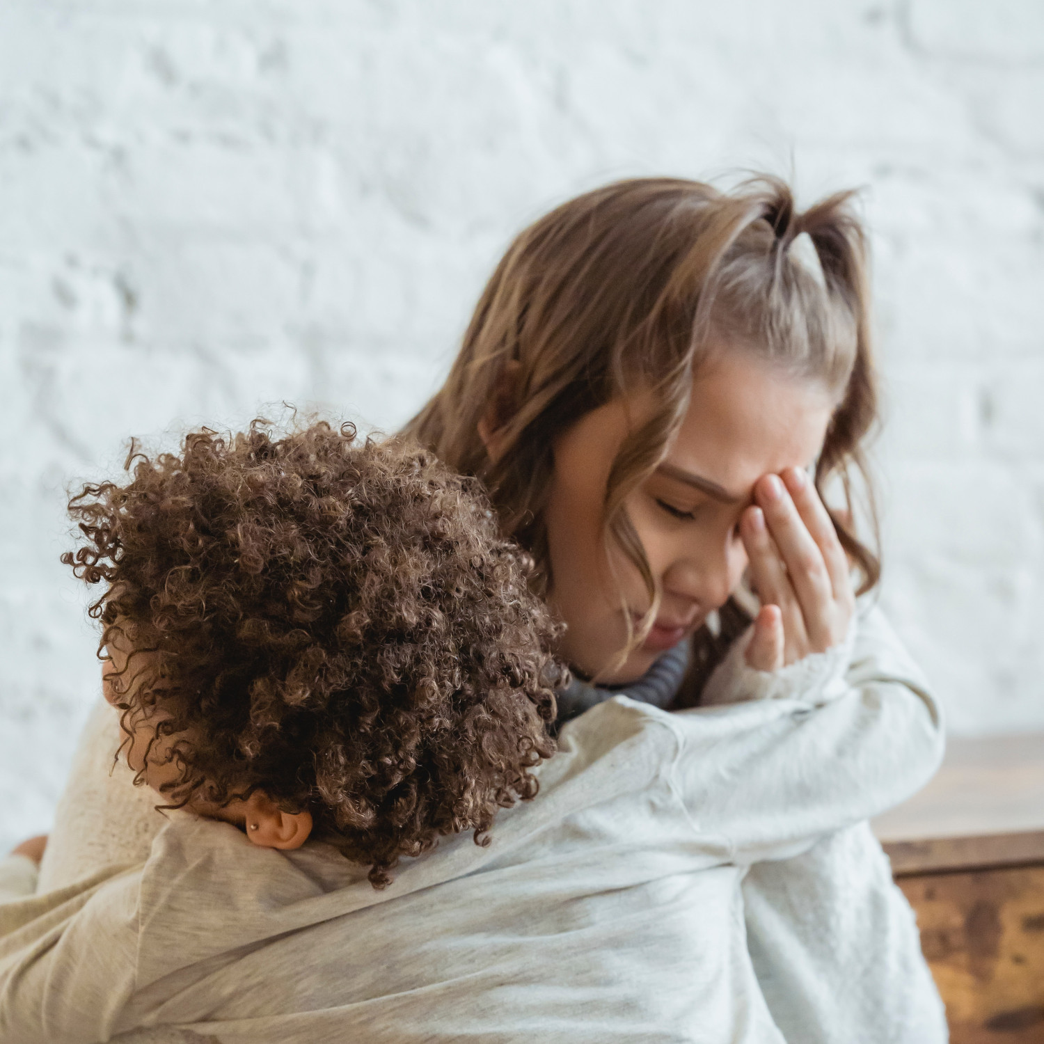 A worried woman is touching her head while hugging her child.