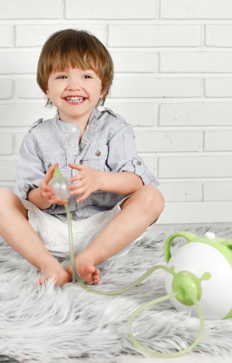 Uśmiechnięty chłopiec trzyma w ręce aspirator elektryczny do nosa Nosiboo Pro