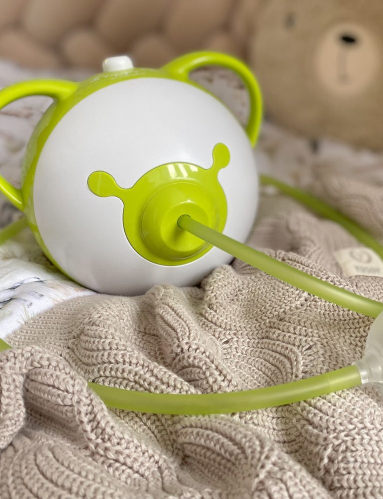 A green Nosiboo Pro2 electric nasal aspirator on a bed.