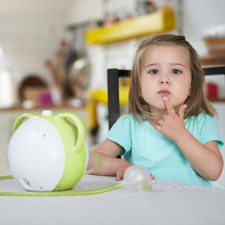 A girl wondering about something, a green Nosiboo Pro electric nasal aspirator next to her on the table